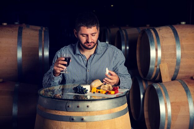 Foto horizontales bild eines kaukasischen mannes, der in einer weingüter sitzt, isst und einen snack isst und ein glas rotwein hält