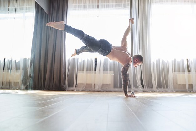 Horizontales Foto eines athletischen Mannes, der viele Übungen auf dem Pylon in der Fitnessklasse des modernen Tanzstudios macht