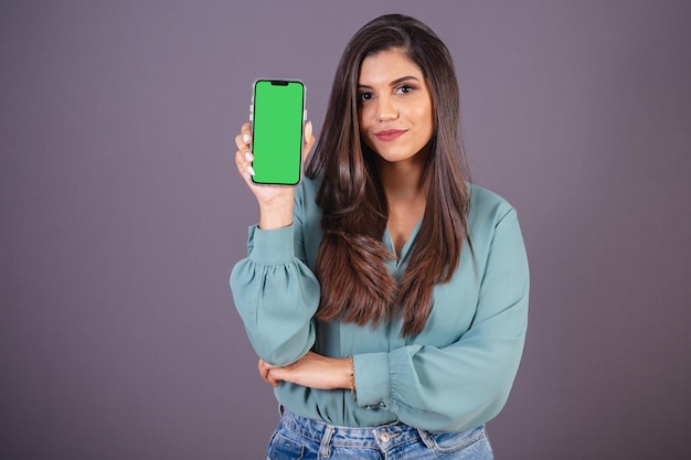 Horizontales Foto Schöne Brasilianerin mit Freizeitkleidung Jeans und grünem Hemd mit Smartphone mit grünem Bildschirm
