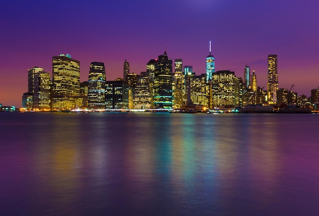 Horizonte de Manhattan à noite com reflexos coloridos na água, Nova York, EUA
