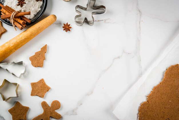 Horneado navideño masa de jengibre para pan de jengibre hombres de pan de jengibre estrellas árboles de navidad rodillo especias (canela y anís) harina en la cocina de la casa mesa de mármol blanco