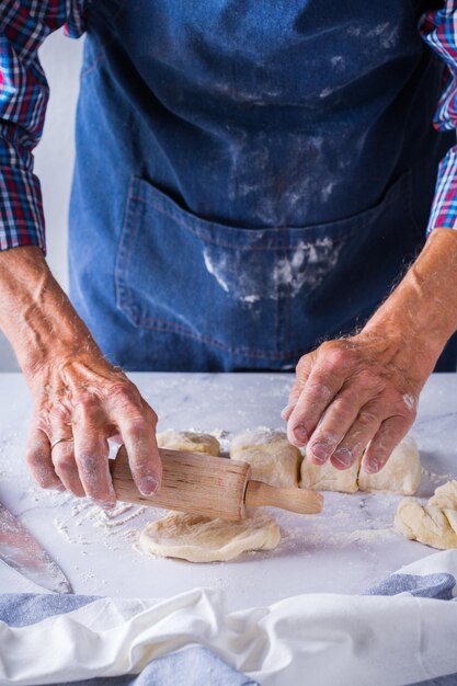 Hornear comer en casa concepto de comida y estilo de vida saludable Panadero senior hombre cocina amasar masa fresca con las manos rodando con alfiler extendiendo el relleno en el pastel en una mesa de cocina con harina