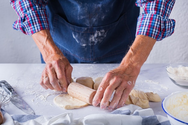 Hornear comer en casa concepto de comida y estilo de vida saludable Panadero senior hombre cocina amasar masa fresca con las manos rodando con alfiler extendiendo el relleno en el pastel en una mesa de cocina con harina