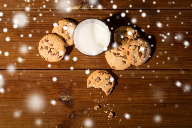 hornear, comer, vacaciones y concepto de comida - cierre de galletas de avena y vaso de leche en la mesa de madera