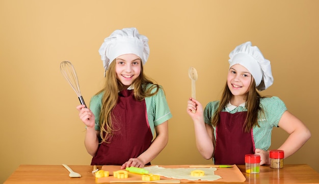 Foto hornear galletas de jengibre niñas hermanas divirtiéndose con masa de jengibre las mejores galletas caseras niños horneando galletas juntos niños delantales y gorros de chef cocinando receta familiar habilidad culinaria educación culinaria