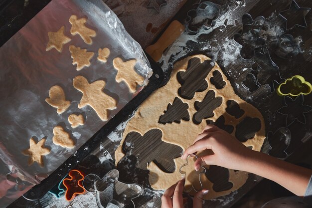 Hornear galletas de Navidad en la mesa de madera de color marrón oscuro. Familia haciendo pan de jengibre, cortando galletas de masa de jengibre, vista desde arriba.