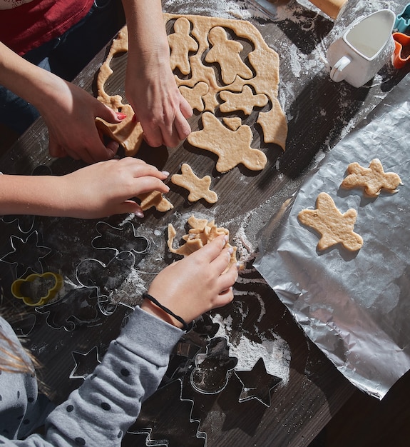 Hornear galletas de Navidad en la mesa de madera de color marrón oscuro. Familia haciendo pan de jengibre, cortando galletas de masa de jengibre, vista desde arriba.