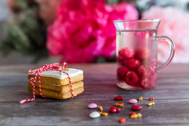 Hornear galletas sorpresa con cobertura y glaseado sobre fondo de madera con corazón rosa y gorra con bebida de malina