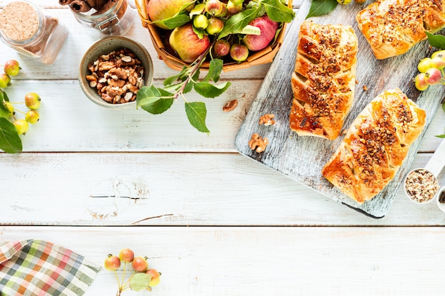 Hornear con manzana, manzana recién horneada y rollos de canela hechos de hojaldre sobre una mesa de madera blanca. Vista superior, estilo rústico, espacio de copia.