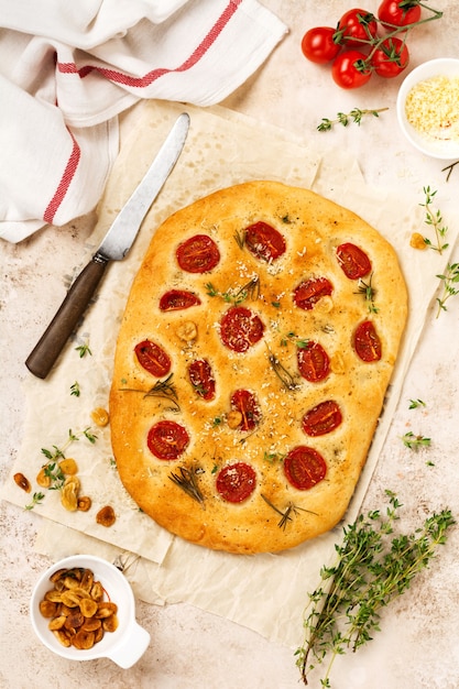 Hornear pan focaccia tradicional italiana con tomates cherry, parmesano y romero sobre fondo marrón claro. Vista superior