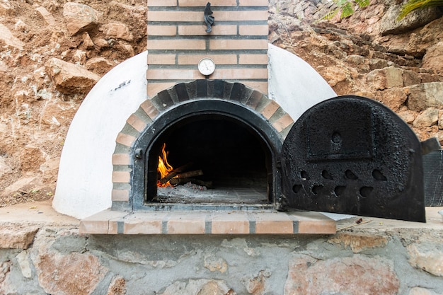 Horno de leña artesanal pintado de blanco con la puerta abierta y fuego en el interior