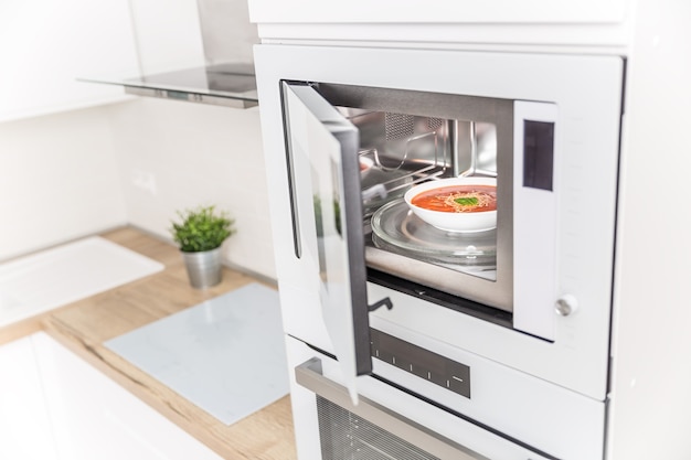 Horno microondas empotrado en la cocina con sopa de tomate en plato blanco.