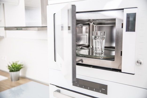 Horno microondas empotrado en la cocina con una taza de agua pura.