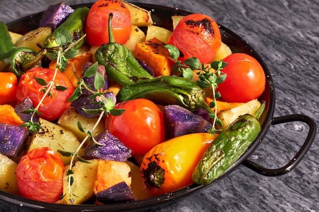 El horno rústico coció verduras en fondo negro de piedra gris de la fuente del horno con el plato. Comida vegetariana estacional vegana