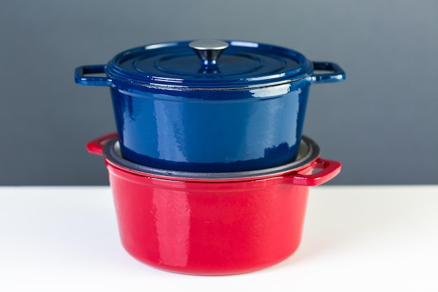 Foto hornos holandeses cubiertos de hierro fundido esmaltado rojo y azul sobre un fondo blanco.