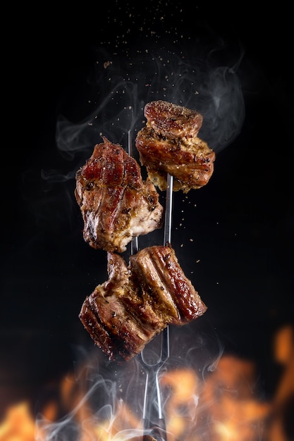 Foto horquilla con trozos de deliciosas carnes a la brasa sobre fondo negro