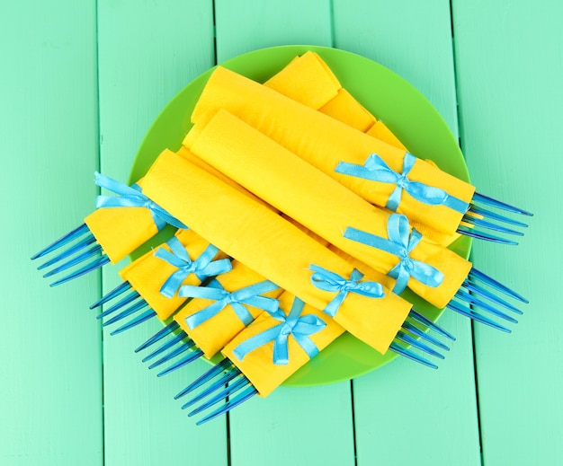 Horquillas de plástico azul envueltas en servilletas de papel amarillo sobre fondo de madera de color