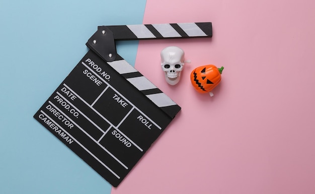 Horrorfilm Halloween-Konzept Film Clapperboard und Schädel mit Jack-o-Lantern-Kopf auf blau-rosa-pastellfarbenem Hintergrund