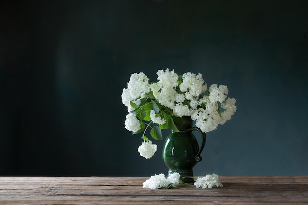 Hortênsia branca em jarro vintage na mesa de madeira na parede escura de fundo