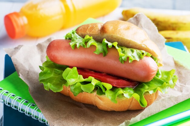 Hot dog con lechuga tomate y salchicha. Cuadernos y papelería. Concepto de escuela Desayuno. Copia espacio