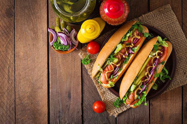 Hot dog con pepinillos, tomate y lechuga sobre superficie de madera