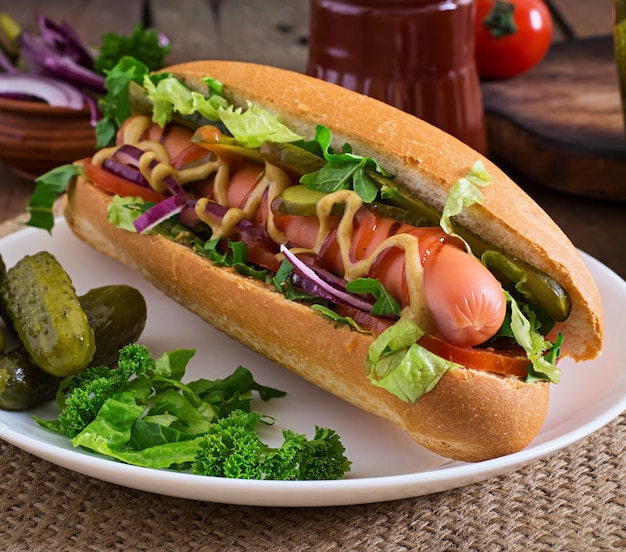 Hot dog con pepinillos, tomate y lechuga sobre superficie de madera