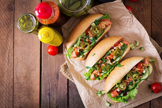 Hot dog con pimientos jalapeños, tomate, pepino y lechuga en mesa de madera