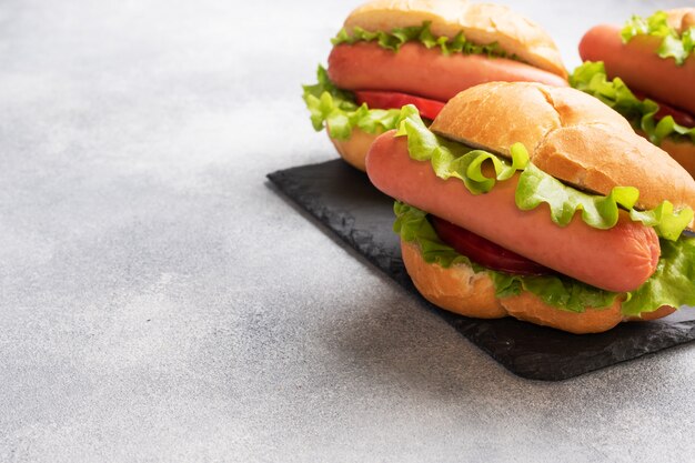 Hot Dogs auf einem konkreten grauen Hintergrund. Hot Dog mit Salattomate und Wurst. Speicherplatz kopieren.
