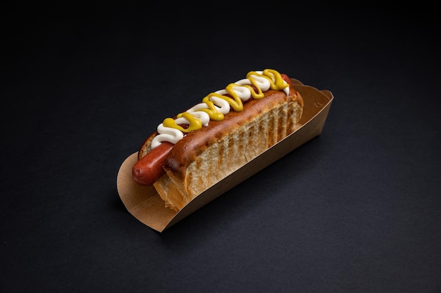 Hot Dogs in Papptellern mit Würstchen und Soße auf schwarzem Hintergrund