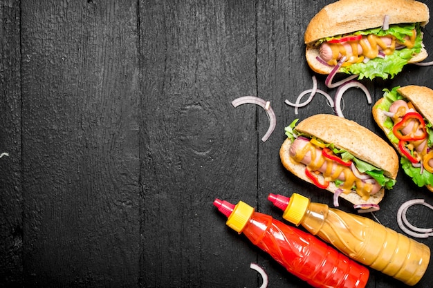 Hot Dogs mit Zwiebeln, Tomaten und heißem Senf auf schwarzer Tafel.