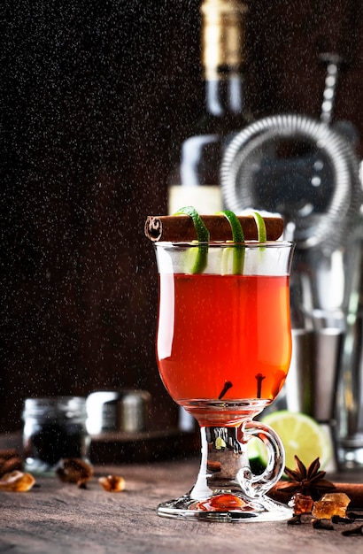 Hot Punch Grog Wintererwärmungscocktail mit dunklem Rum Port Honig Limettensaft Tee Zimt und Nelken im Glas auf Vintage-Holzhintergrund in Herbstdekoration