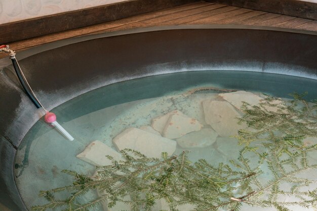 Hot Tub mit Thermometer im Inneren und vielen umherschwimmenden Kiefernzweigen Felsen am Boden Entspannend Ausruhen Gesundheit Person Resort Rückzugsbad Sauna Lifestyle Alpine Hot Tub Freiheit Schön