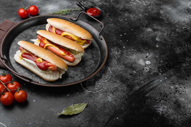 Hotdog-Grillwurst in einem Brötchen mit Saucen auf schwarzem, dunklem Steintischhintergrund mit Kopierraum für Text