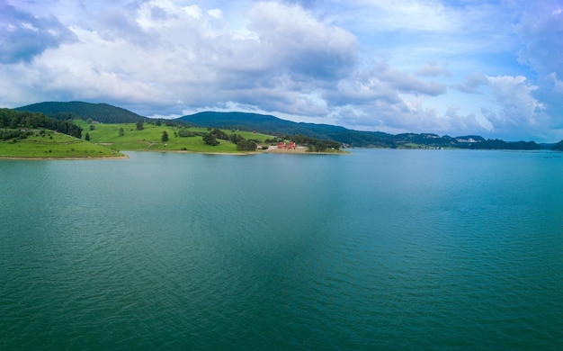 Hotéis nas margens do lago com reflexo das montanhas rhodope contra a vista superior do panorama do céu nublado