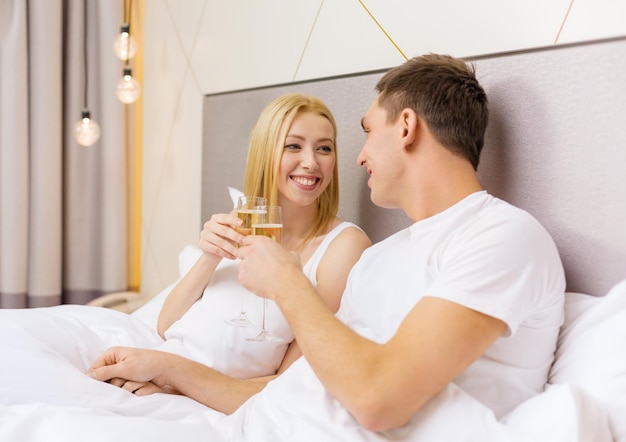 hotel, viajes, relaciones y concepto de felicidad - pareja sonriente con copas de champán en la cama