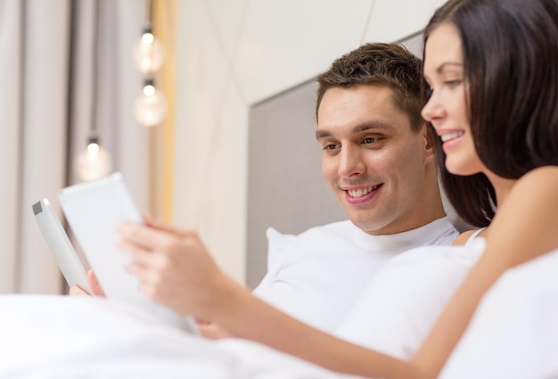 hotel, viajes, relaciones, tecnología, intermet y concepto de felicidad - pareja sonriente en la cama con tabletas