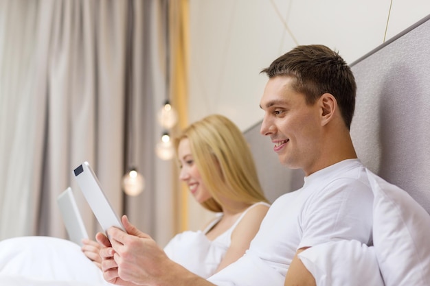 hotel, viajes, relaciones, tecnología, intermet y concepto de felicidad - pareja sonriente en la cama con tabletas