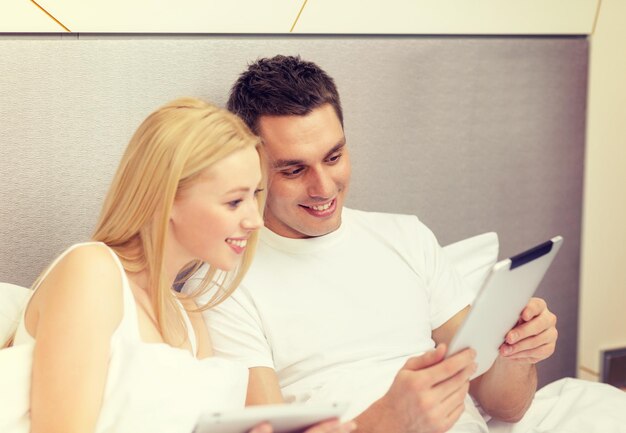 hotel, viajes, relaciones, tecnología, intermet y concepto de felicidad - pareja sonriente en la cama con tabletas