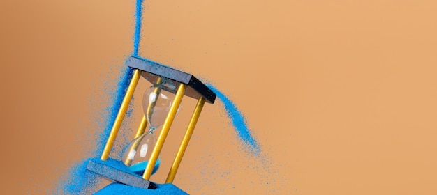 Hourglass ist Geld Sand der Zeit Geschäft gießen blauen Sand in Hourglass, um mehr Zeit in der finanziellen Frist erweitert Zeitmanagement Hoffnung Konzept zu Gold Stunde Glas Orange Hintergrund Sonnenuntergang