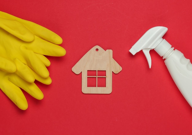 Housekeeping-Konzept. Satz von Produkten zur Reinigung (Handschuhe, Sprühflasche) und Hausfigur auf rotem Hintergrund. Draufsicht.