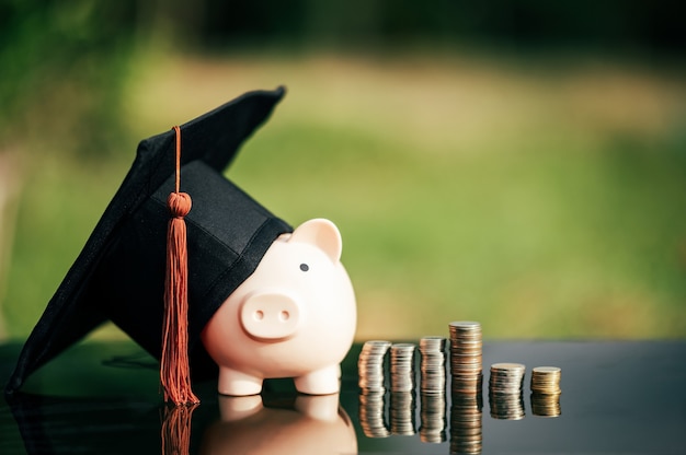 Hucha con gorro de graduación en piso de vidrio negro, concepto de ahorro de dinero.