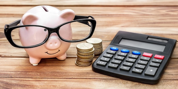 Hucha con monedas y calculadora en mesa de madera Concepto financiero