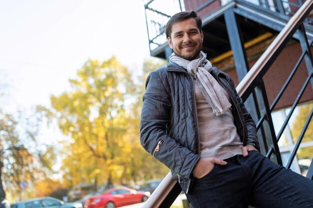 Hübsch mit einem stilvollen jungen Mann, der sich vor dem Hintergrund der Herbststadt auf die Treppe lehnt