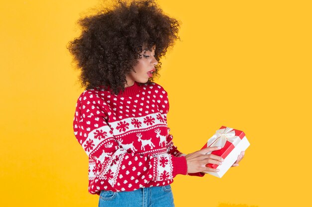 Hübsche afroamerikanische Frau, im neuen Jahr Weihnachten, mit einem Geschenk in der Hand, gelber Hintergrund