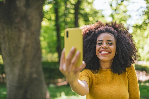 Hübsche Afrofrau, die ein selfie lächelnd im Wald nimmt. Selektiver Fokus.