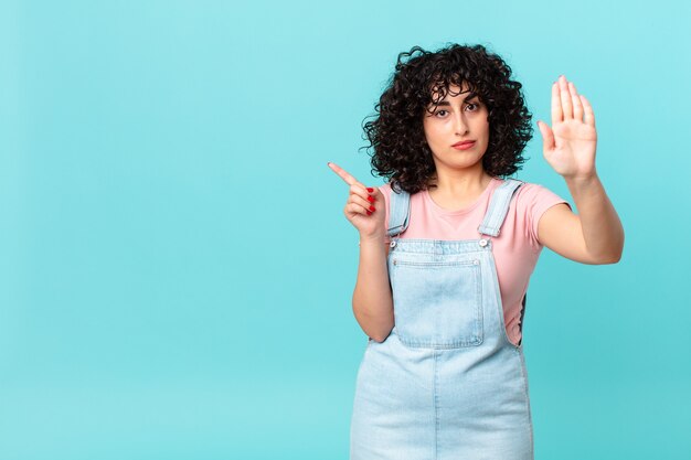 Hübsche arabische Frau, die ernst aussieht und offene Handfläche zeigt, die Stopp-Geste macht