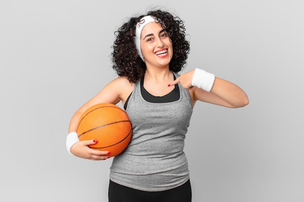 Hübsche arabische frau, die sich glücklich fühlt und auf sich selbst zeigt, mit einem aufgeregten und ein basketballball-sportkonzept