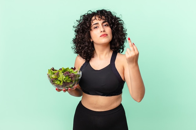 Hübsche arabische Frau, die sich wütend, genervt, rebellisch und aggressiv fühlt und einen Salat hält. Diät-Konzept