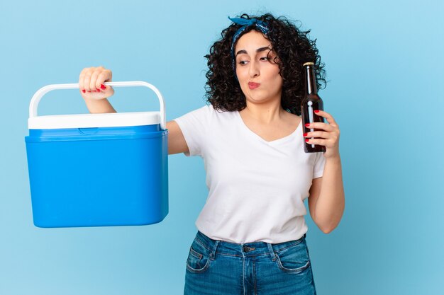 Hübsche arabische frau mit einem tragbaren kühlschrank und einem bier