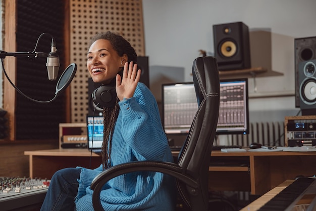 Hübsche Archorwoman-Radiomoderatorin grüßt, während sie in einem Rundfunk- und Tonaufnahmestudio in ein Mikrofon spricht